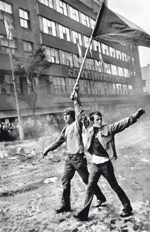 Dva mladíci nesou československou vlajku před rozstříleným rozhlasem v Praze. Snímek pořídil fotograf Josef Koudelka