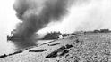Hořící vyloďovací člun a kanadští padlí na pláži u Dieppe