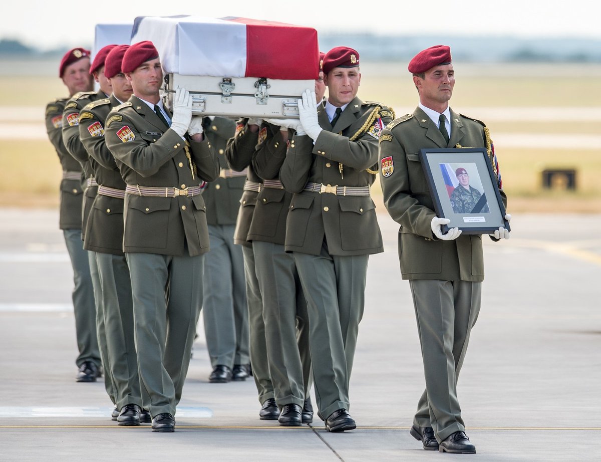 Rakve s ostatky těl vynesli vojáci postupně na letištní plochu. V čele šel voják nesoucí fotografii padlého