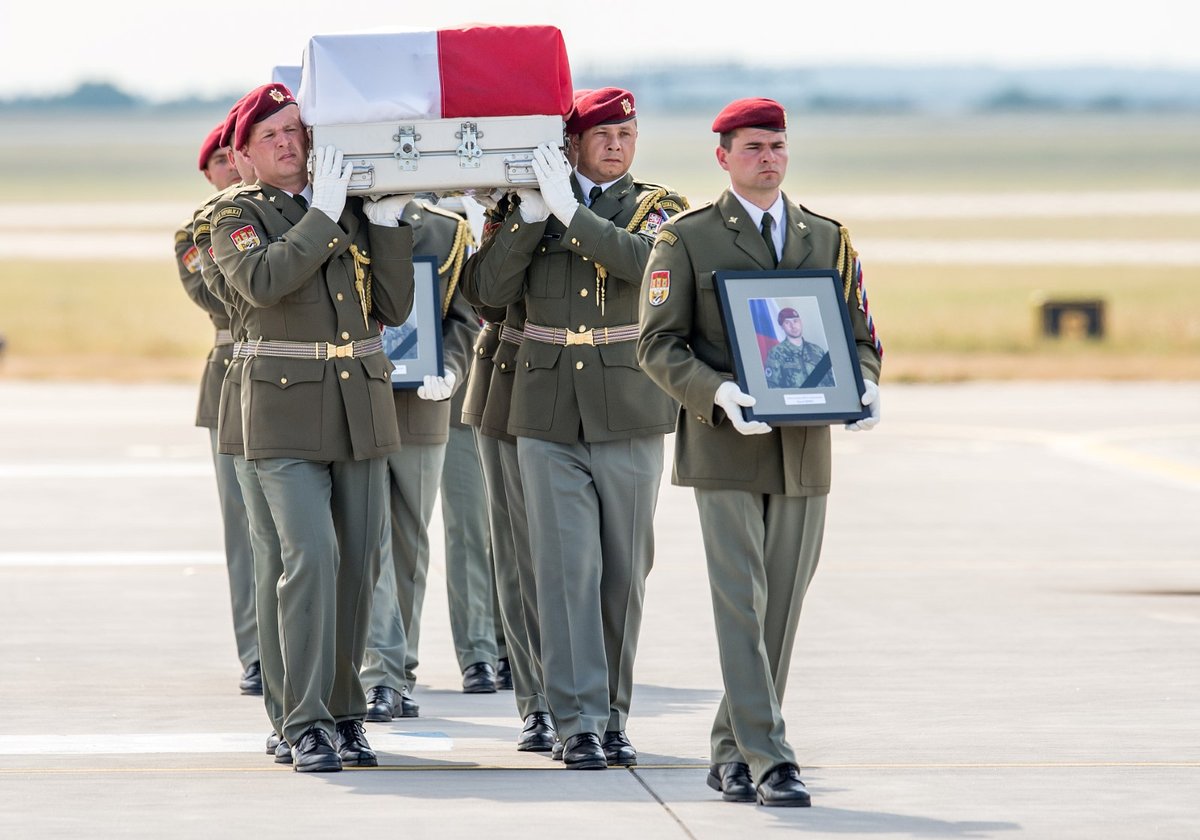 Rakve s ostatky těl vynesli vojáci postupně na letištní plochu. V čele šel voják nesoucí fotografii padlého