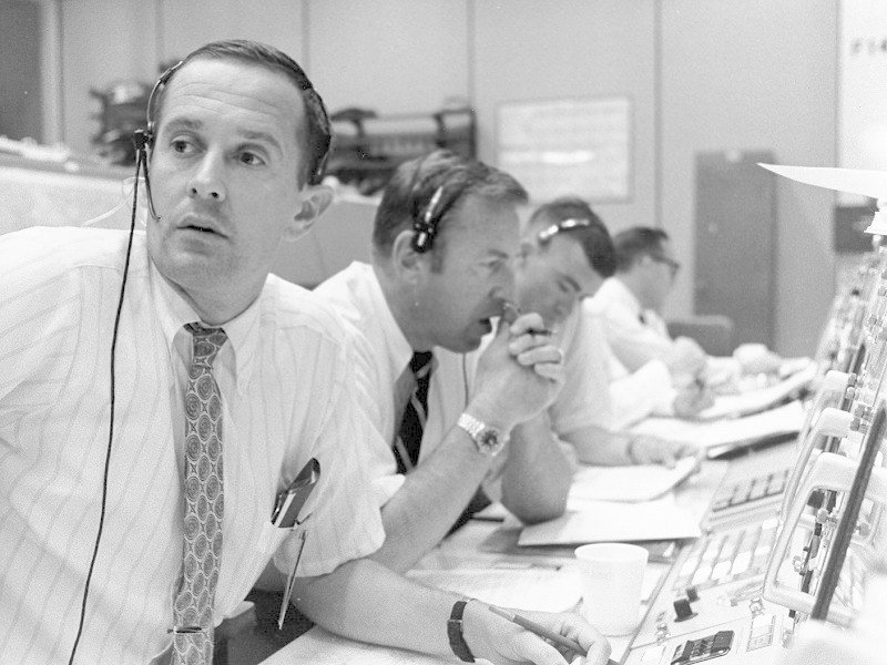 V řídicím středisku seděli také astronauti. Na obrázku je Charles Duke v roli tzv. Capcomu, což je člověk, který komunikoval přímo s posádkou. Dále jsou na snímku Jim Lovell a Fred Haise, kteří byli záložní posádkou Apolla 11