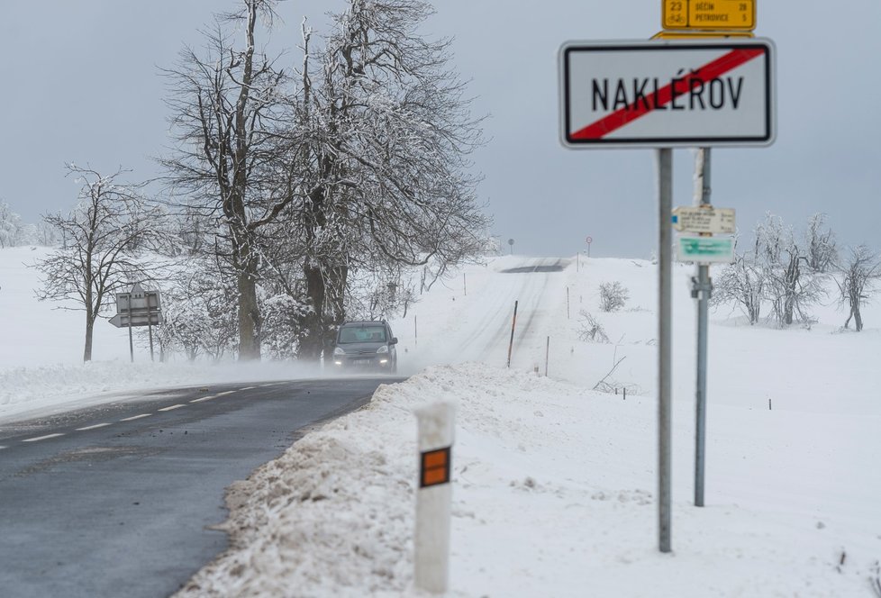 Auto projíždí po zasněžené silnici u Nakléřova na Ústecku (13. 1. 2021).