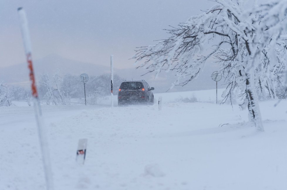 Auto projíždí po zasněžené silnici u Nakléřova na Ústecku (13. 1. 2021)