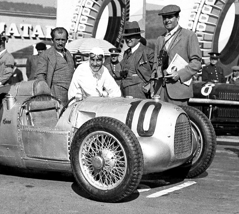 Hans Stuck s vozem Auto Union Typ A po vítězství na Velké ceně Československa v roce 1934 na brněnském Masarykově okruhu. Ferdinand Porsche stojí vlevo od Hanse Stucka.