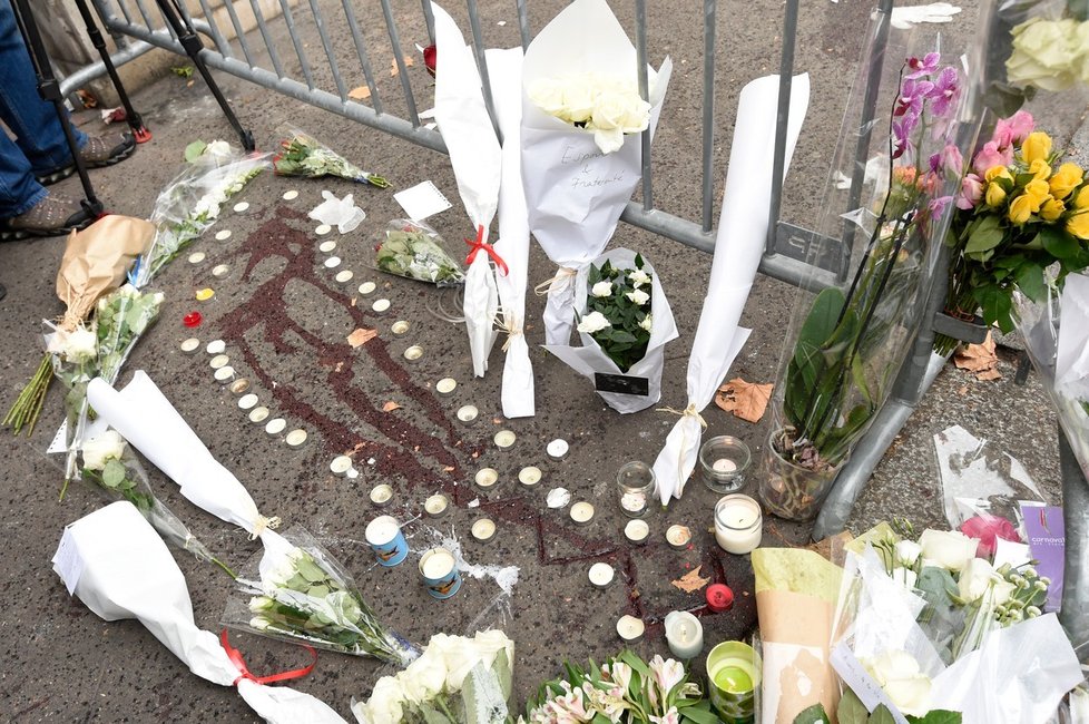 Vedle koncertní haly Bataclan se přes zaschlou krev hromadí květiny a svíčky. Lidé uctívají památku padlých.