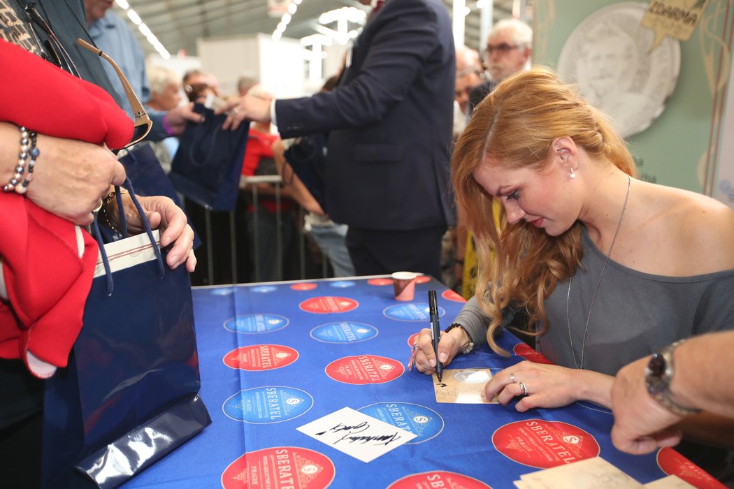 Gabriela Koukalová se podepisuje na autogramiádě u příležitosti uvedení Muchových medailí, ke kterým vytvořila motiv