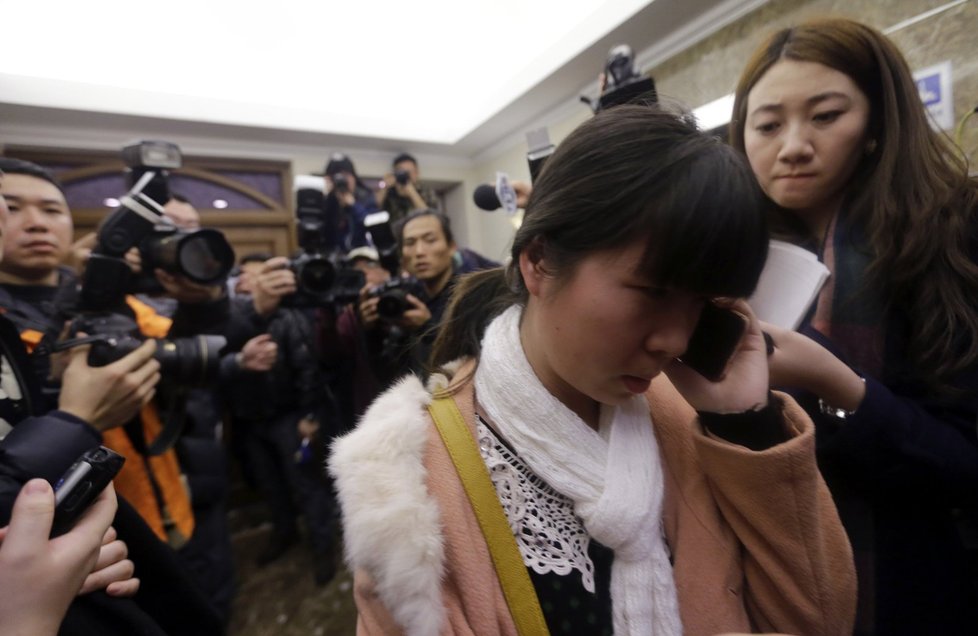 Příbuzná některého z pasažérů malajsijských aerolinek telefonuje, zatímco ji dav novinářů fotografuje.