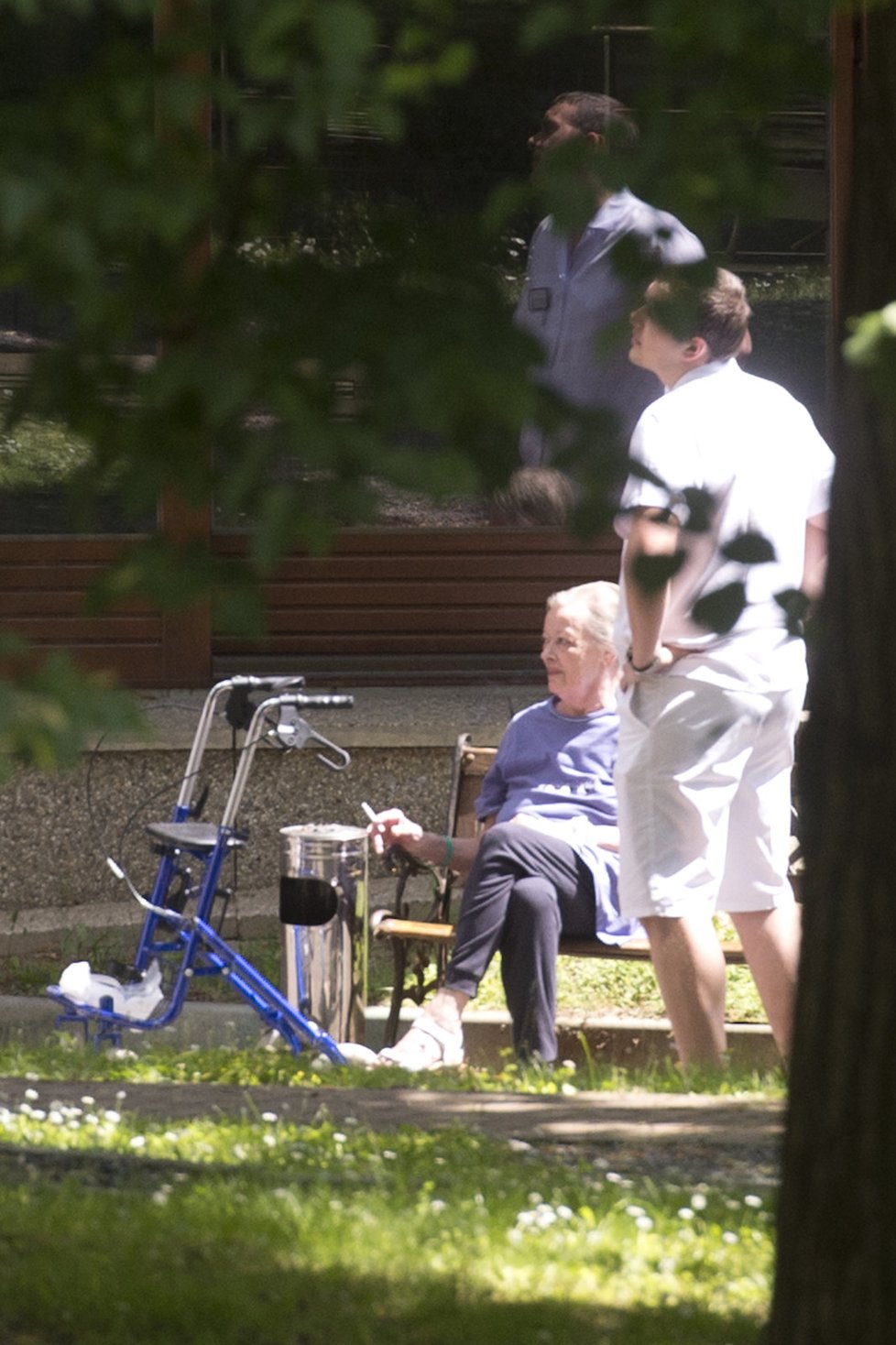 Brejchovou na procházce po zahradě kliniky doprovází chodítko a fyzioterapeut.