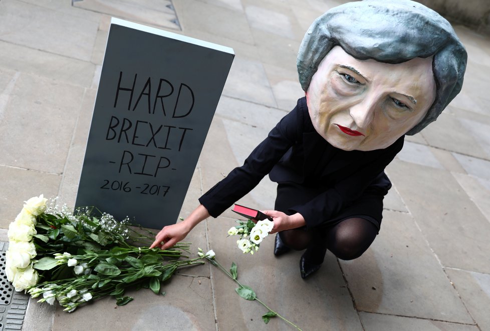 Demonstrantka v masce Mayové klade květiny na hrob brexitu.