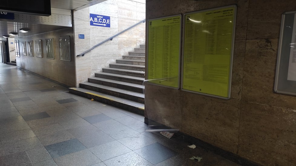 Poničená informační tabule a povalující se odpadky v podchodu pod nástupišti na brněnském hlavním nádraží.