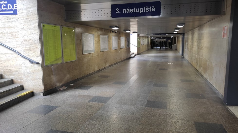 Poničená informační tabule a povalující se odpadky v podchodu pod nástupišti na brněnském hlavním nádraží.