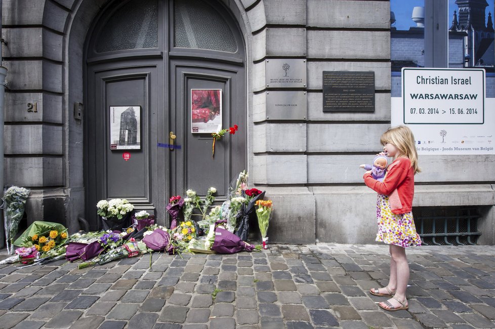 Dívka stojí před dveřmi židovského muzea v Bruselu, kam lidé položili květiny.