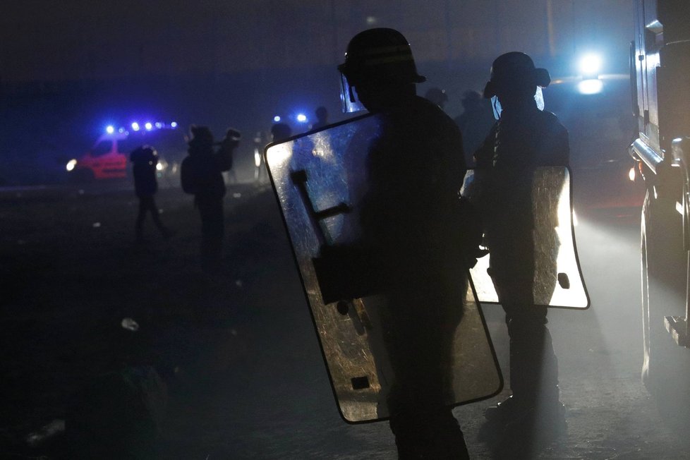 Policisté zasahují proti migrantům, kteří založili požár v táboře v Calais.
