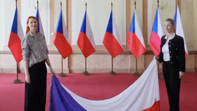 Česká vlajka dotýkající se země. Drží ji mluvčí vlády Karla Mráčková a členka PR hnutí ANO Aneta Zicklerová.