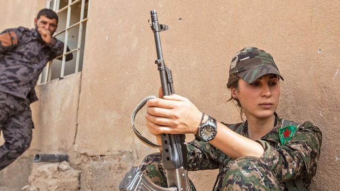 Chaos. Kurdská bojovnice Zelan Dirbeseyová patří k řadám syrských levicových jednotek YPJ. Na kurdských územích v Sýrii, kde jsme společně pracovaly na frontové linii, vládne dost nepřehledná situace. Oblast ovládá levicově orientovaná milice YPG, v podstatě odnož známější PKK (Kurdské strany pracujících), jež působí v Iráku. Portréty společného vůdce Abdulláha Očalana visí všude včetně rozbitých lamp veřejného osvětlení. Rudé hvězdy doplňují i podobizny mučedníků, kteří padli za svou ideologii. YPG ale spolupracuje také i s režimem Bašára Asada a bojuje proti další z kurdských stran PDK, podporované Masúdem Barzáním z Iráku. Na kurdské oblasti navíc útočí Islámský stát, operuje tam i šíitské hnutí
Hizballáh podporované Íránem a svou roli hraje také Fronta an-Nusrá.