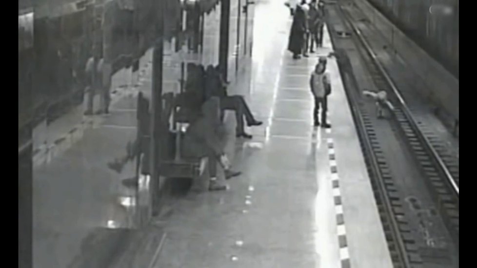 Muž skáče do kolejiště za chlapcem.