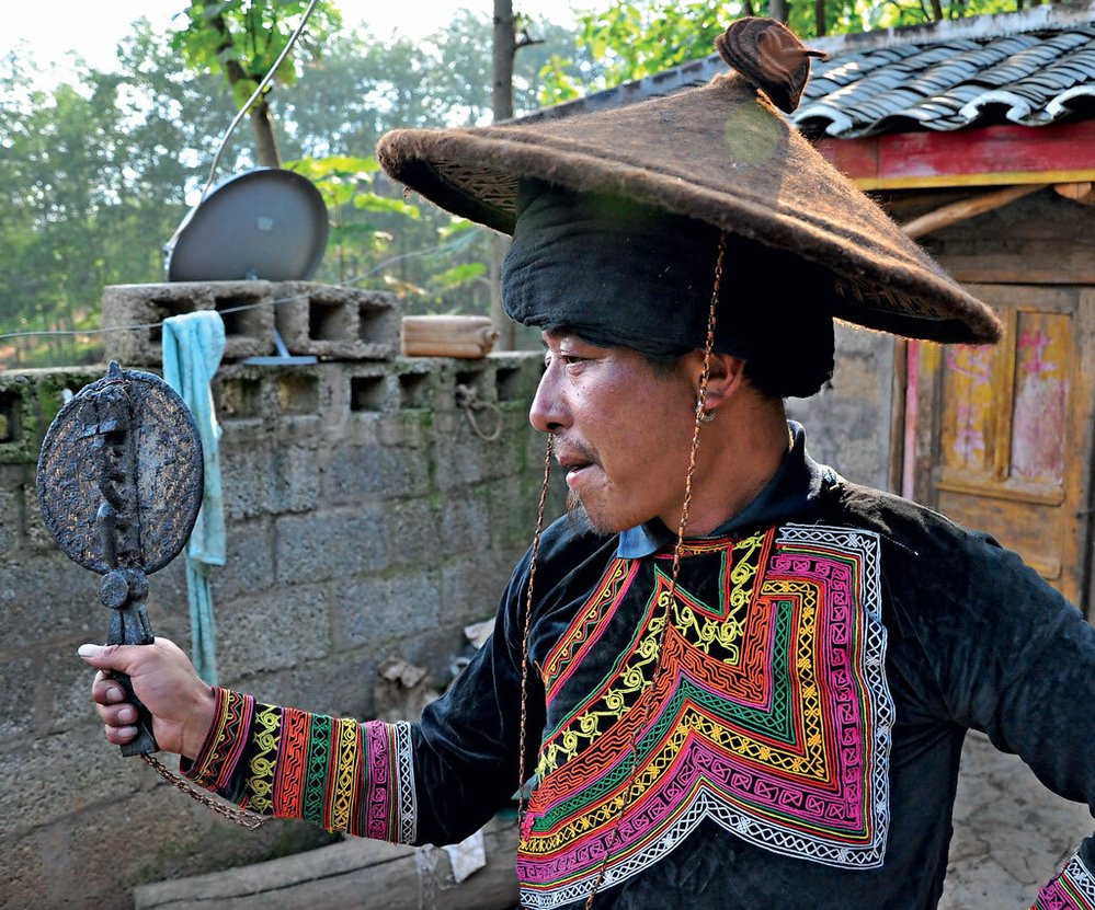 Pi-mo ve svém tradičním obleku, s kloboukem kuhle a vějířem vytu. Vše tvoří nepostradatelnou část výzbroje učence z hor.