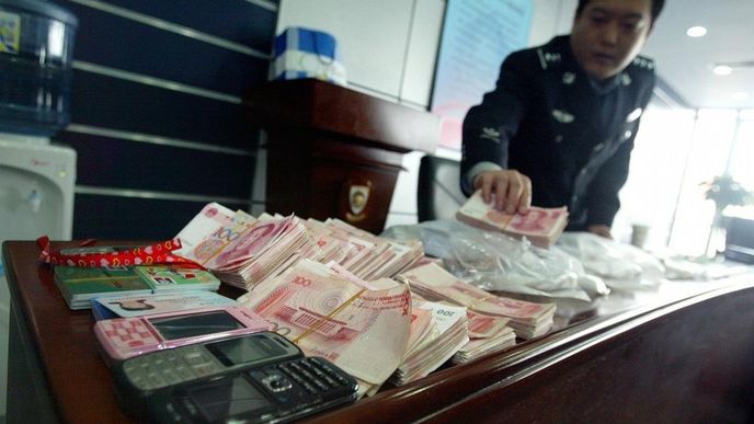 Čínský policista ukazuje peníze a další předměty zabavené během razie