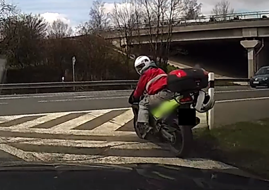 Motorkář zastavuje na křižovatce a ohlíží se po policejním autě.