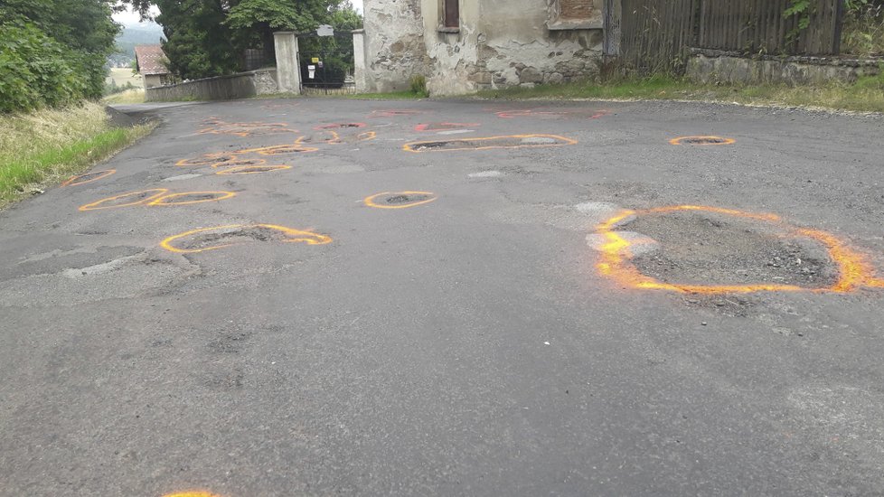 Rozbitá silnice v Krásné Lípě na Sokolovsku. Místní díry omalovali reflexní barvou.