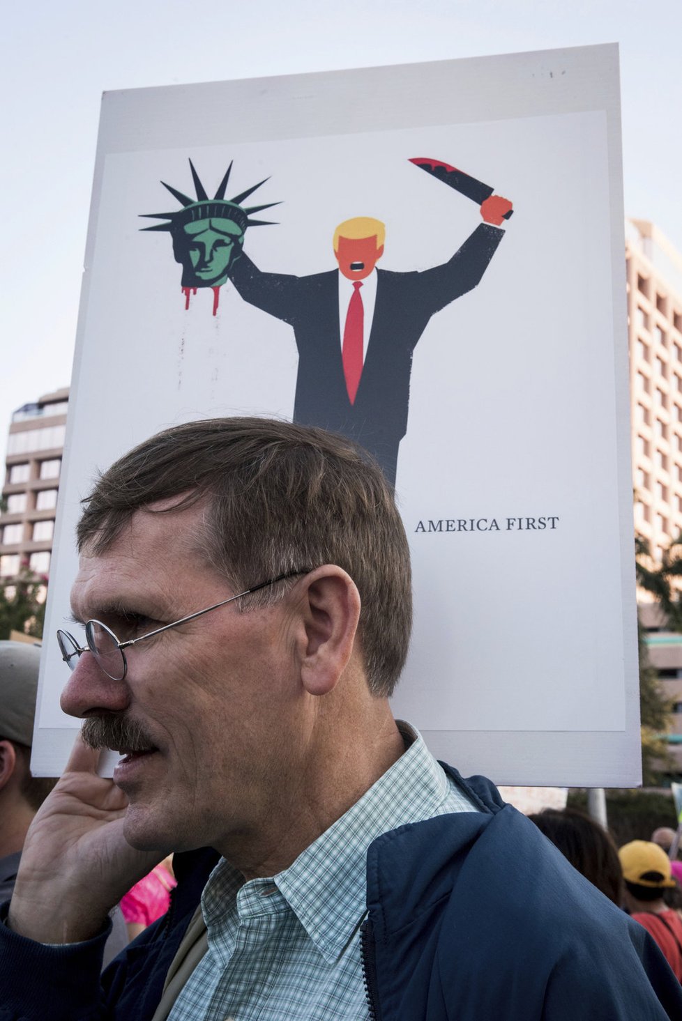 Muž protestující před holdingem Donalda Trumpa. V pozadí zvětšenina karikatury, kterou otiskl německý deník Der Spiegel. Znázorňuje Trumpovu popravu demokracie.