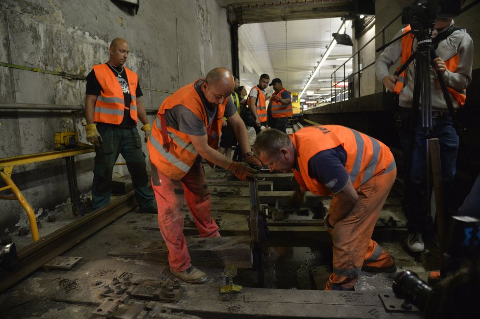 Dělníci v tunelu metra odstraňují dřevěné pražce z kolejiště.