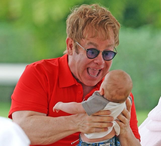 Elton předvádí, jak by podle něj měla vypadat otcovská láska, chlapeček z toho ale příliš velkou radost nemá.