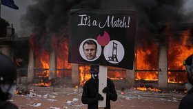 Demonstrant drží transparent s fotografií francouzského prezidenta Emmanuela Macrona a gilotinou před hořící turistickou informační kanceláří během protestů proti rostoucím životním nákladům a na podporu studentů ve francouzském Lyonu (17. 10. 2026)