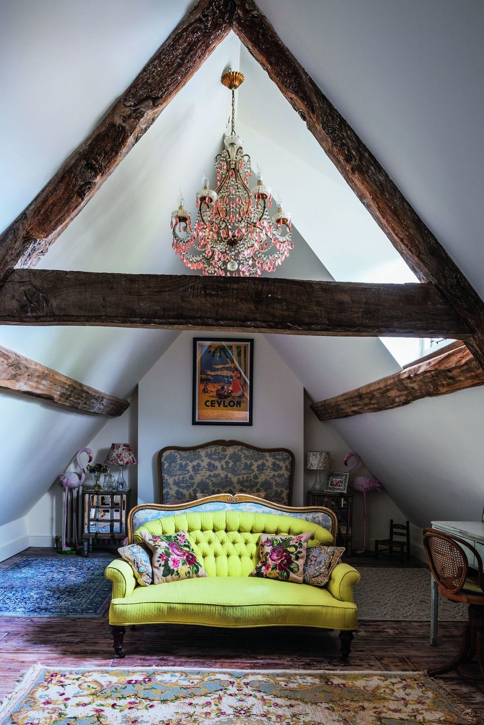 Zámecké sofa a výrazný růžový křišťálový lustr zajímavě kontrastují s přiznanými krovy.