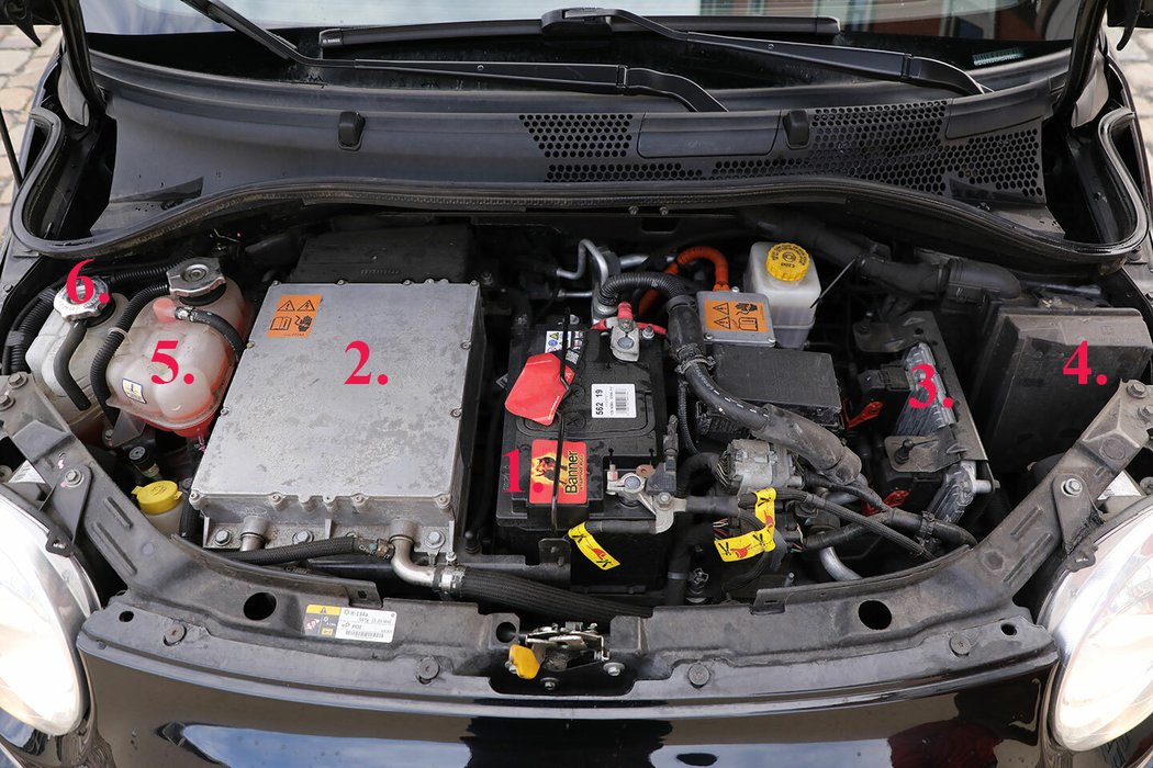 Pod kapotou se kromě 12V baterie 1 ukrývá palubní nabíječka 2 , řídící jednotka 3 , primární pojistková skříň 4 , nádoba chladicí kapaliny 5 pro chladicí okruh motoru a výkonové elektroniky a nádoba chladicí kapaliny 6 pro okruh baterie.