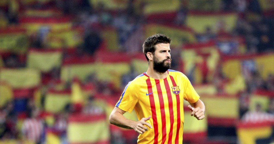 Obránce Barcelony Gerard Piqué při rozcvičení v katalánském dresu svého týmu. Za ním záplava španělských vlajek na tribunách stadionu Atlética.