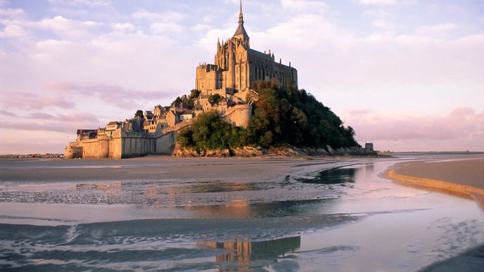 Mont-Saint-Michel. Monumentální klášter okupující vrcholek 80 metrů vysokého ostrůvku uprostřed zálivu, který se během přílivu plní vodou, píše svou historii dle legend již od osmého století. Tehdy zde biskupu Aubertovi ve zjevení přikázal postavit modlitebnu sám archanděl Michael. Hora svatého Michala je dnes ikonickou památkou celé Normandie.