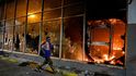 Bezdomovec běží vedle hořící banky, když během protestů proti policejní brutalitě v kolumbijské Cali propukly střety