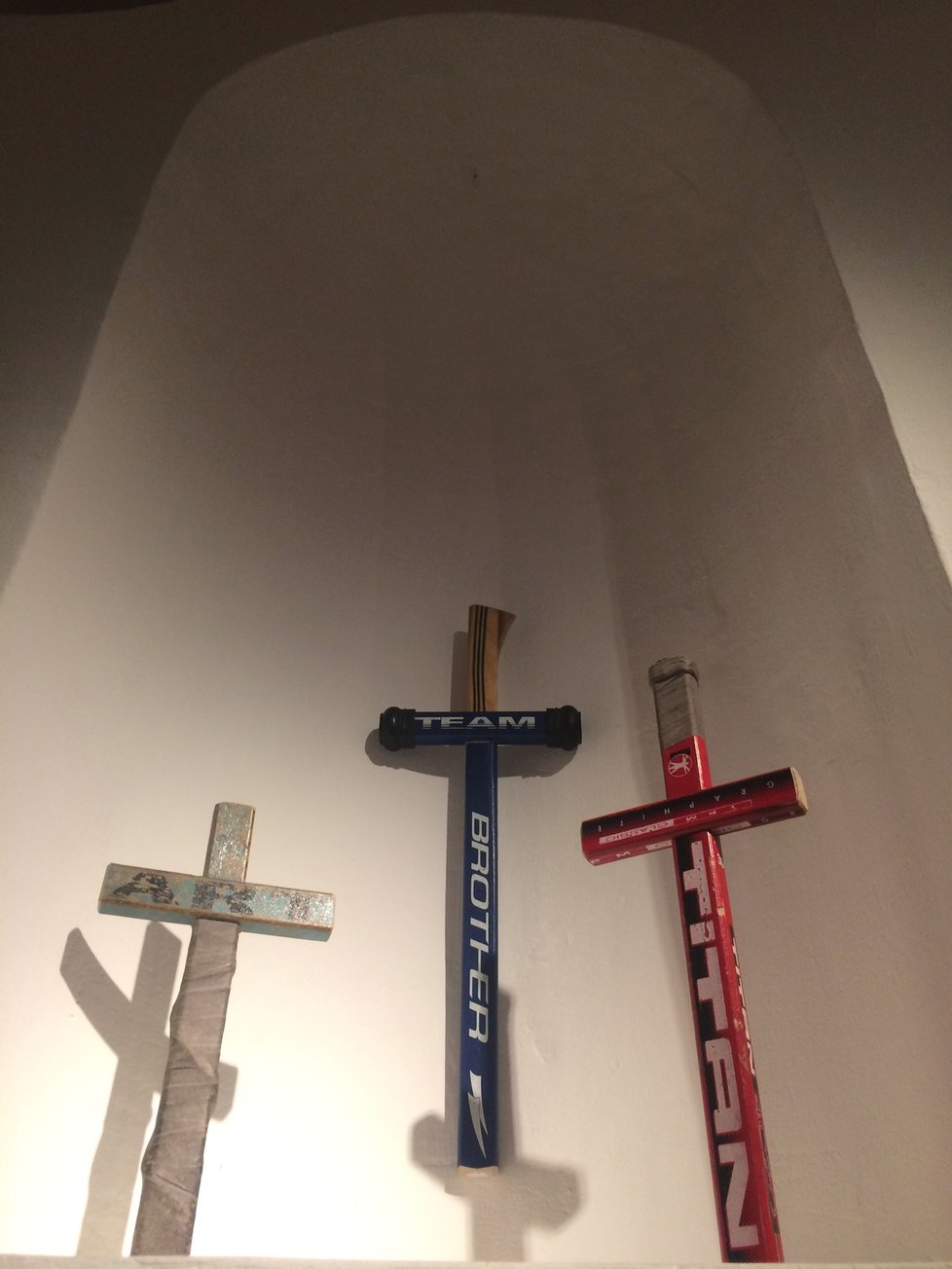 Někdy k umění stačí málo. Třeba vzít hokejku a udělat z ní kříž, tedy náboženský posvátný symbol. Přesně tak i působí ve výklenku, do nějž je instalace usazena.
