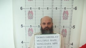 Guru Jára po zatčení. Policista před ním drží cedulku s nápisem „Dobeš Jaroslav, mnohonásobné znásilnění“