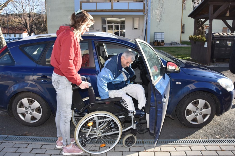 Invalida František Havlík (74) vystupuje z auta. Na vozík mu pomáhá Dana Jílková (51).