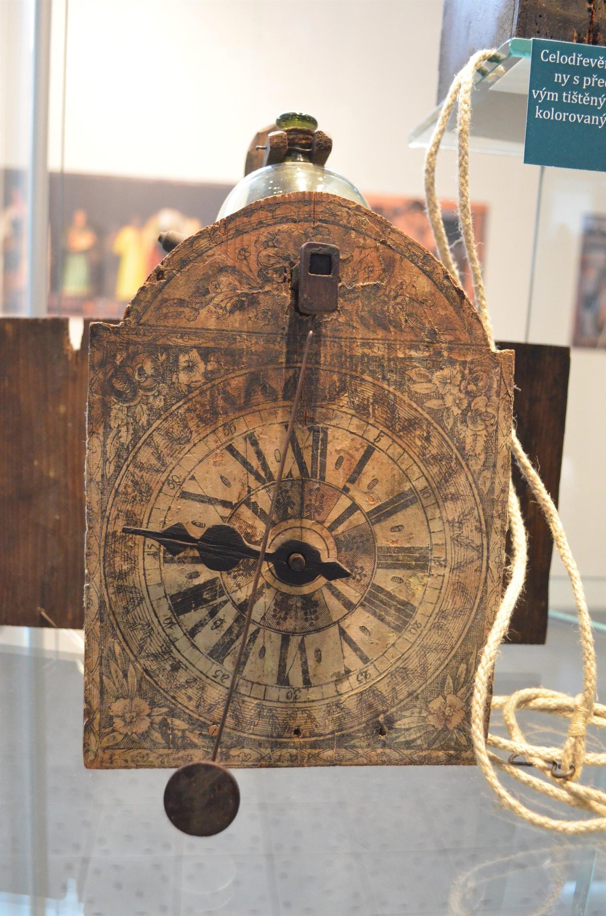 Celodřevěné jednoručičkové hodiny s předním kyvadlem a papírovým tištěným číselníkem z konce 18. století.
