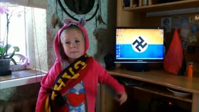 Na monitoru za dívenkou svítí koláž z vlajky Ukrajiny a hákového kříže.