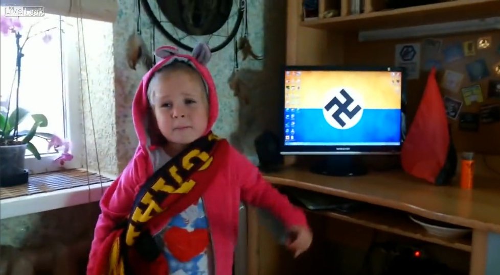 Na monitoru za dívenkou svítí koláž z vlajky Ukrajiny a hákového kříže.