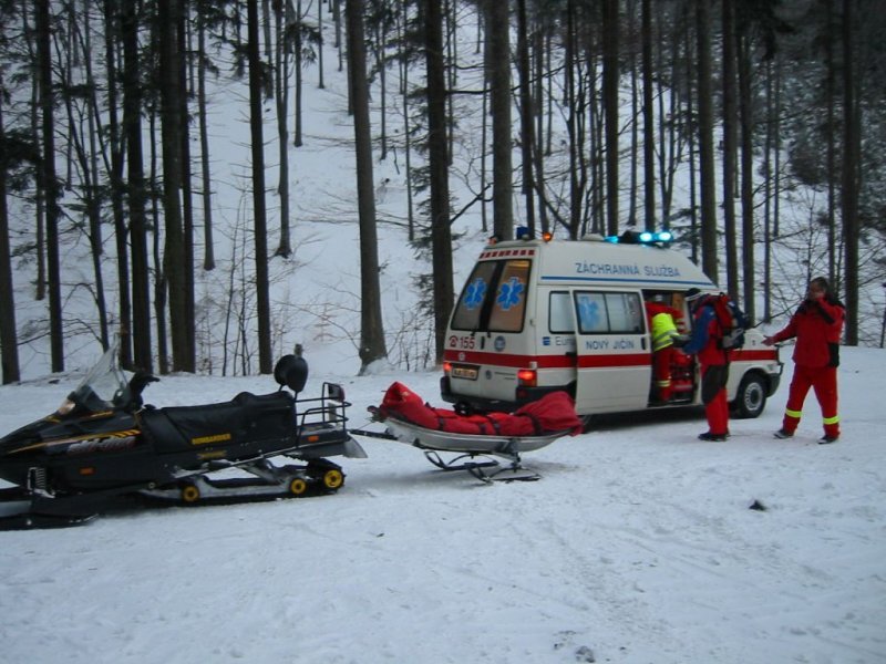 Teď už je lyžař z nejhoršího venku, záchranáři jej předávají posádce sanitky.