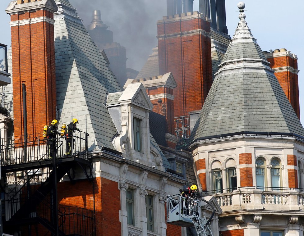 Více než stovka hasičů bojuje s požárem luxusního hotelu v centru Londýna. Ze střechy budovy stoupá hustý dým.