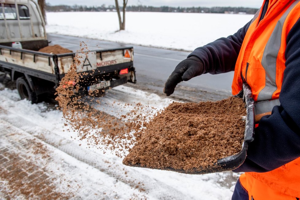 Pracovník technických služeb v Hradci Králové sype písek na zasněženou dlažbu autobusové zastávky (13. 1. 2020)