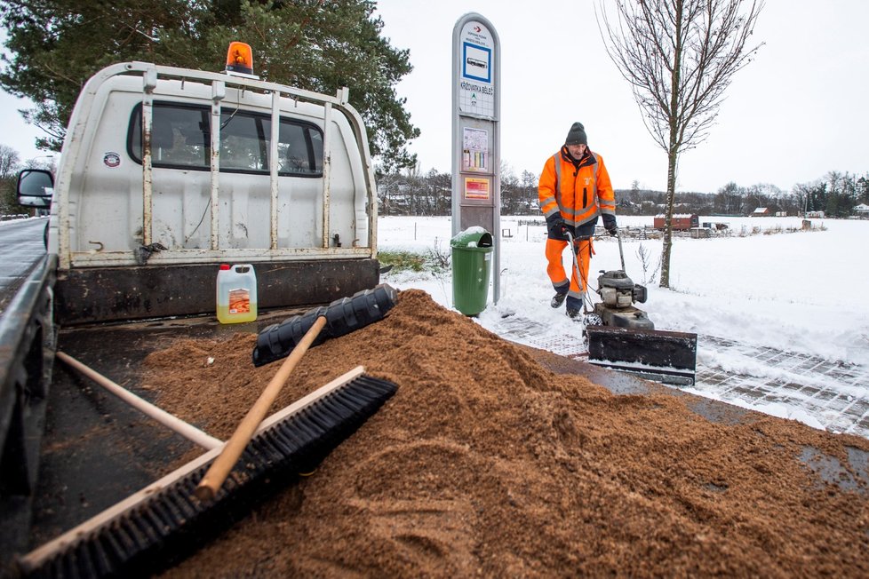 Pracovník technických služeb v Hradci Králové odklízí sníh z dlažby autobusové zastávky (13. 1. 2020)