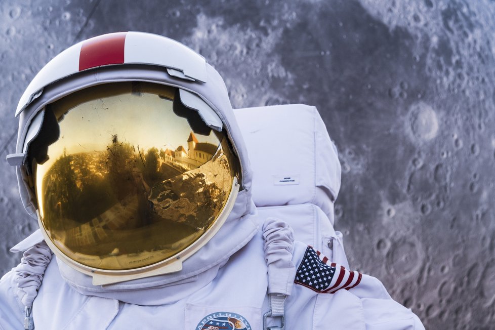 Brněnská hříčka. Astronaut stojí u modelu Měsíce a v hledí přilby se mu zobrazuje hrad Špilberk.