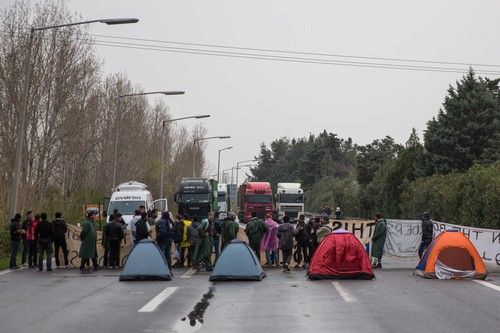 Uprchlíci si i s dětmi polehali na dálnici. V pozadí jsou transparenty se vzkazem: „Otevřete hranice“.