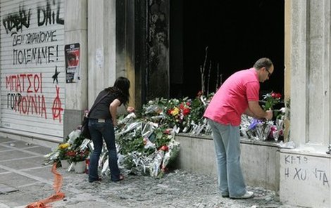 Lidé včera pokládali květiny k bance, kterou ve středu zapálili demonstranti. Mezi třemi oběťmi byla i žena v pokročilém stadiu těhotenství.