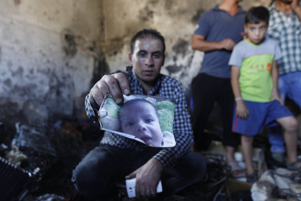 Příbuzný ukazuje foto 18měsíčního Aliho, který uhořel při útoku izraelských radikálů.