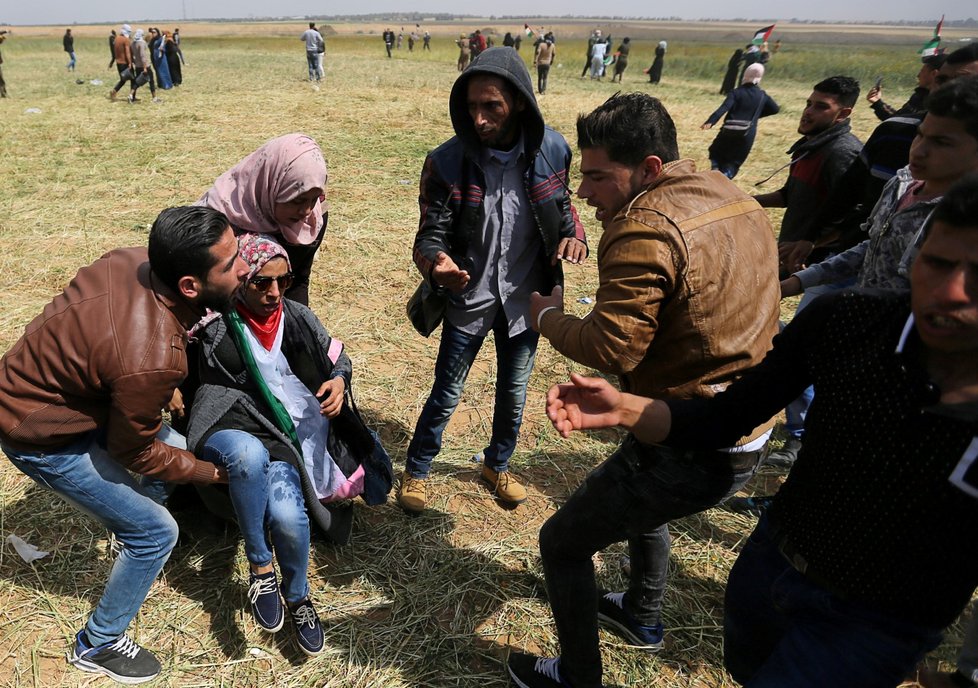 Protestující Palestinci na hranicích pásma Gazy odnáší zraněnou ženu.
