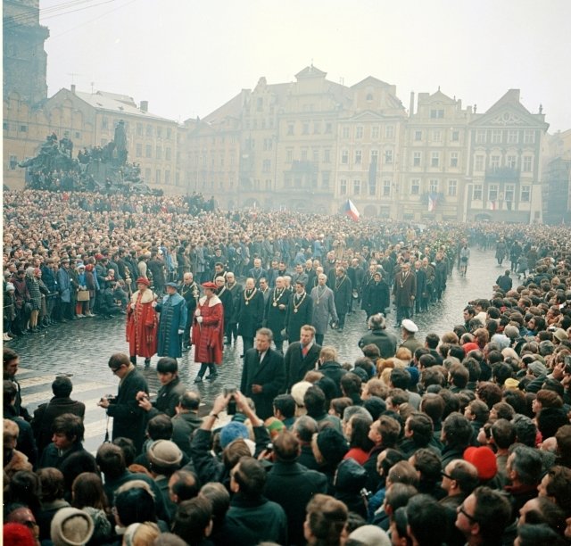 Pohřební průvod za rakví Jana Palacha prochází mezi davy lidí na Staroměstském náměstí. V průvodu jdou hodnostáři Karlovy univerzity.