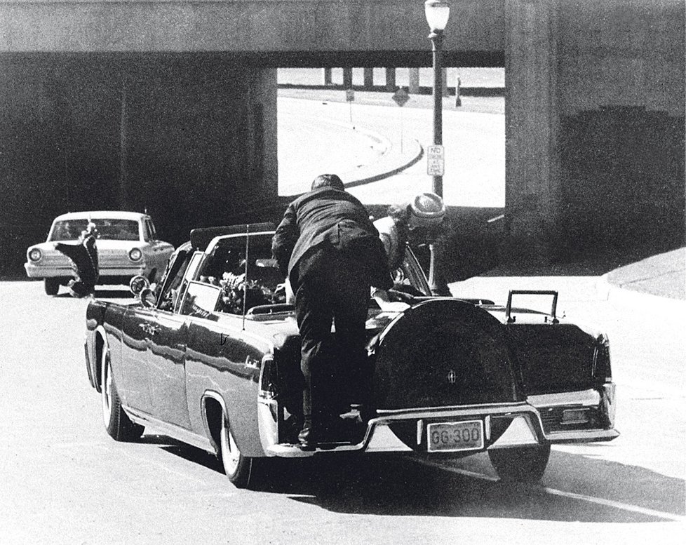 JFK zasáhly dvě kulky. Jeho žena Jackie vstává a volá: „Zabili mi muže! Držím v ruce jeho mozek!“